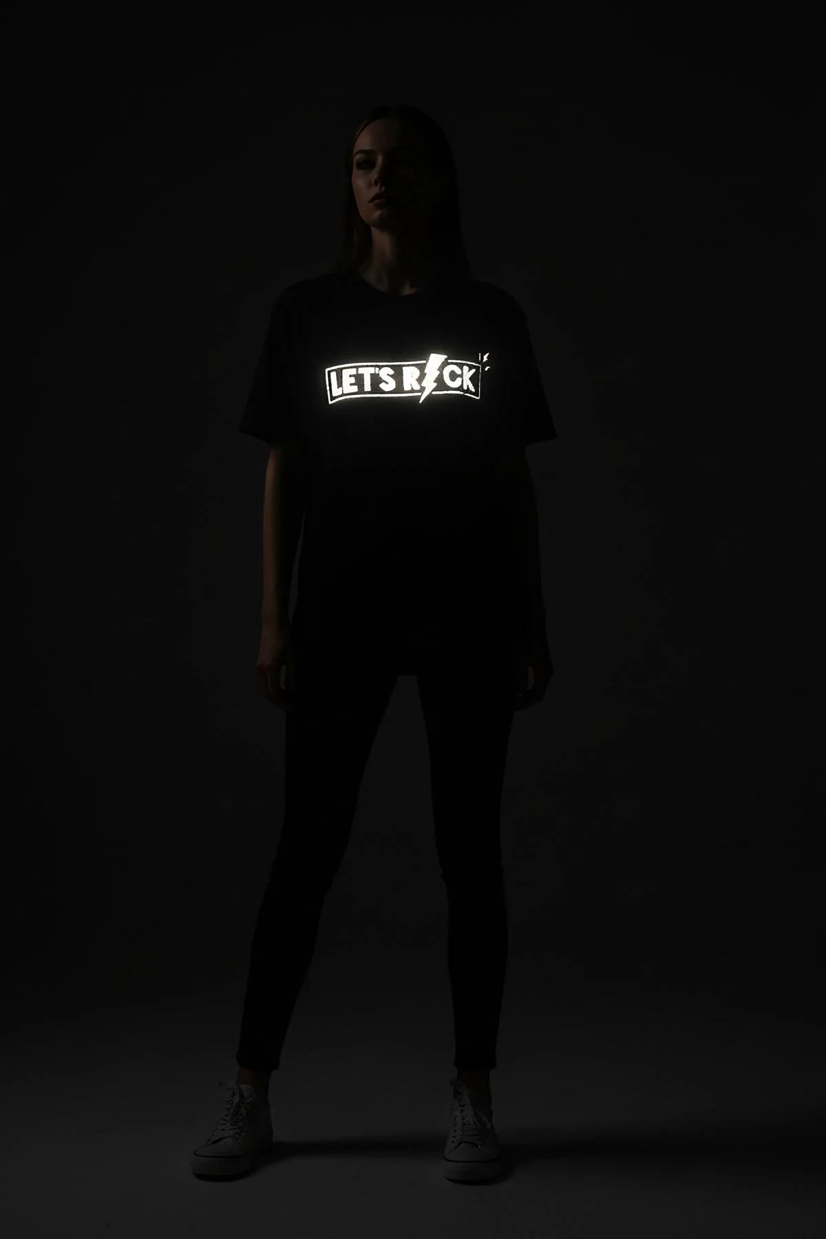 black reflective graphic t-shirt with Let's Rock lightning bolt print glowing silver-white under light, relaxed boxy fit