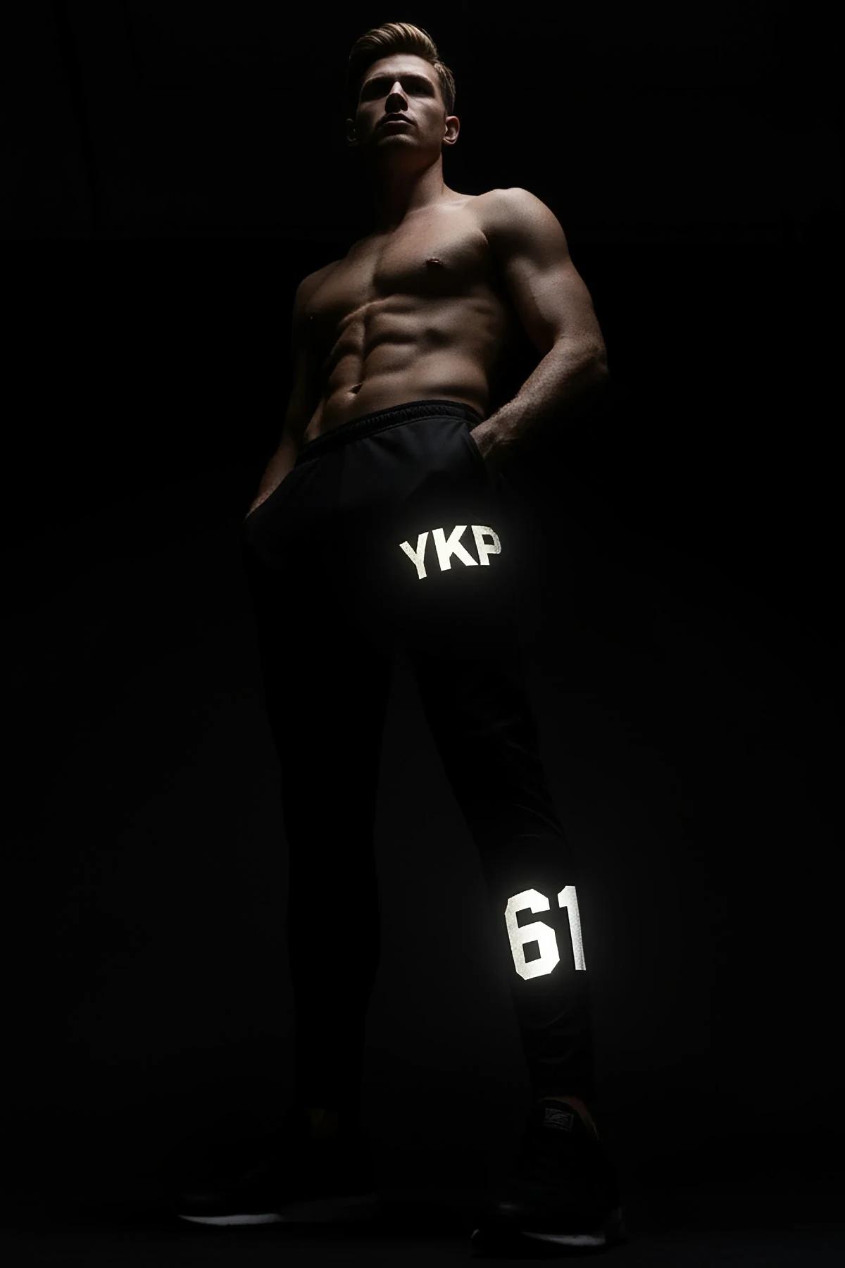 close-up of retroreflective MRT logo on black jogger thigh panel under direct flash