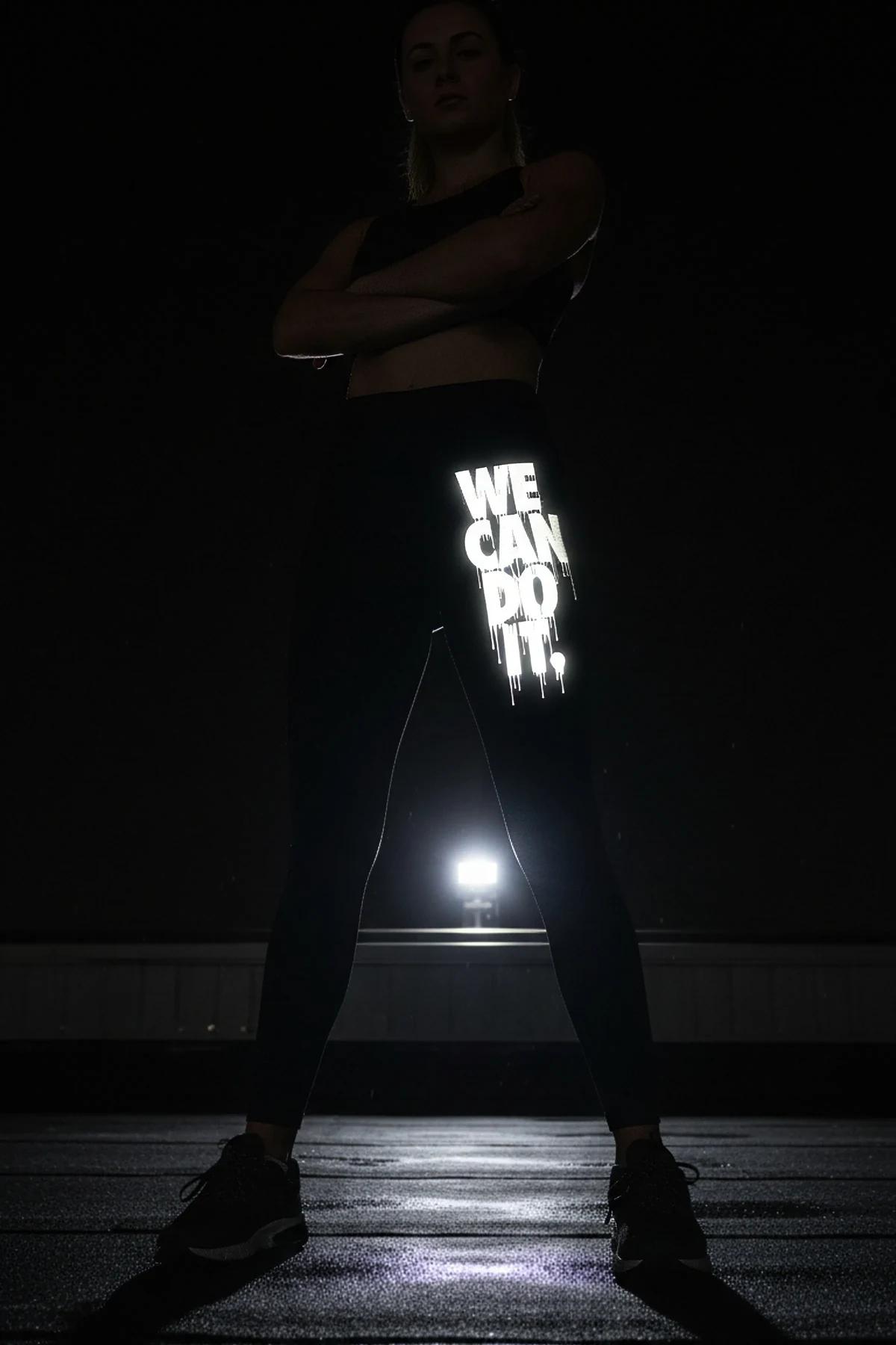 close-up of reflective We Can Do It drip lettering on black legging left thigh in direct light