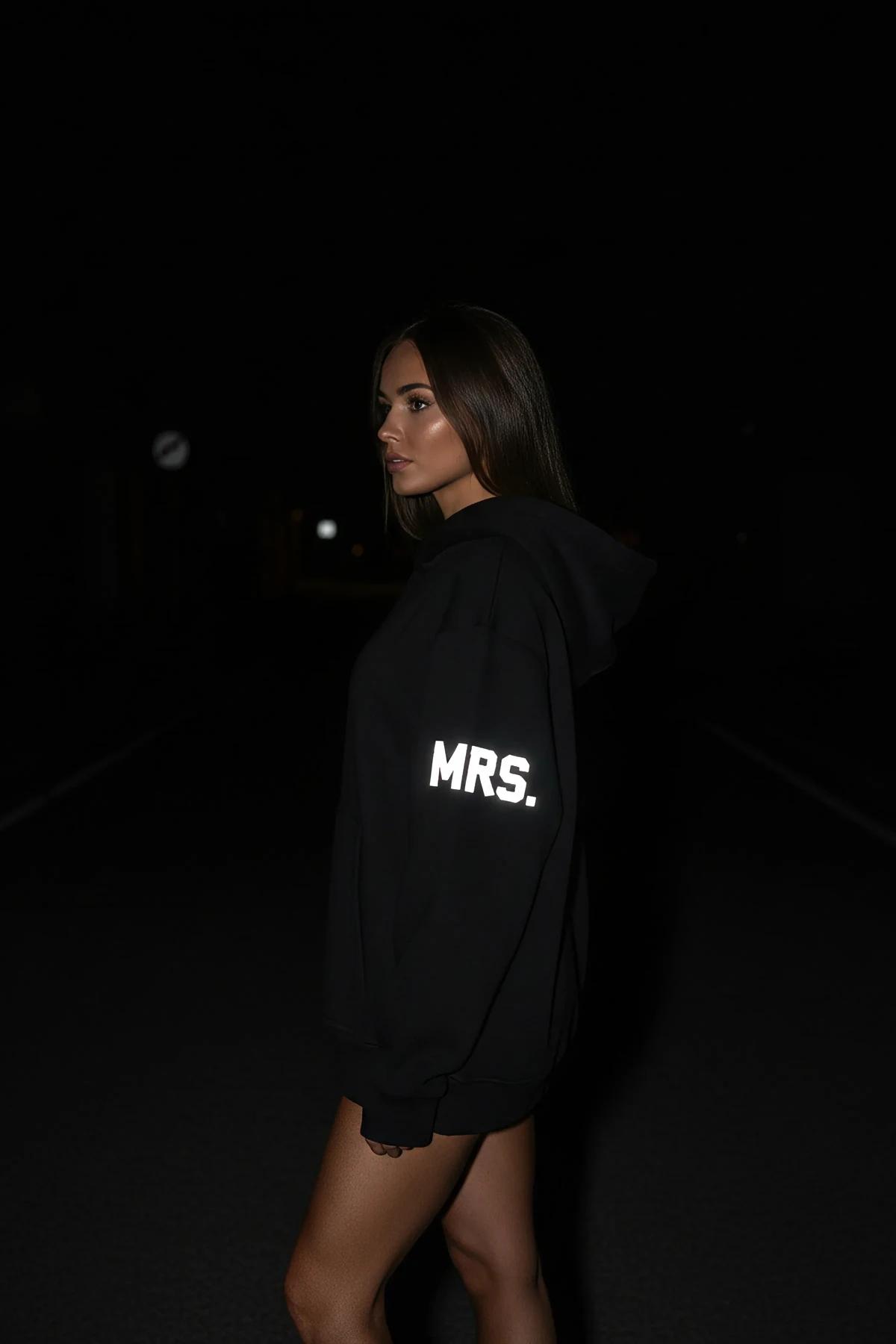 black oversized Mrs. hoodie with white reflective glow-in-the-dark MRS. block-letter sleeve print photographed at night