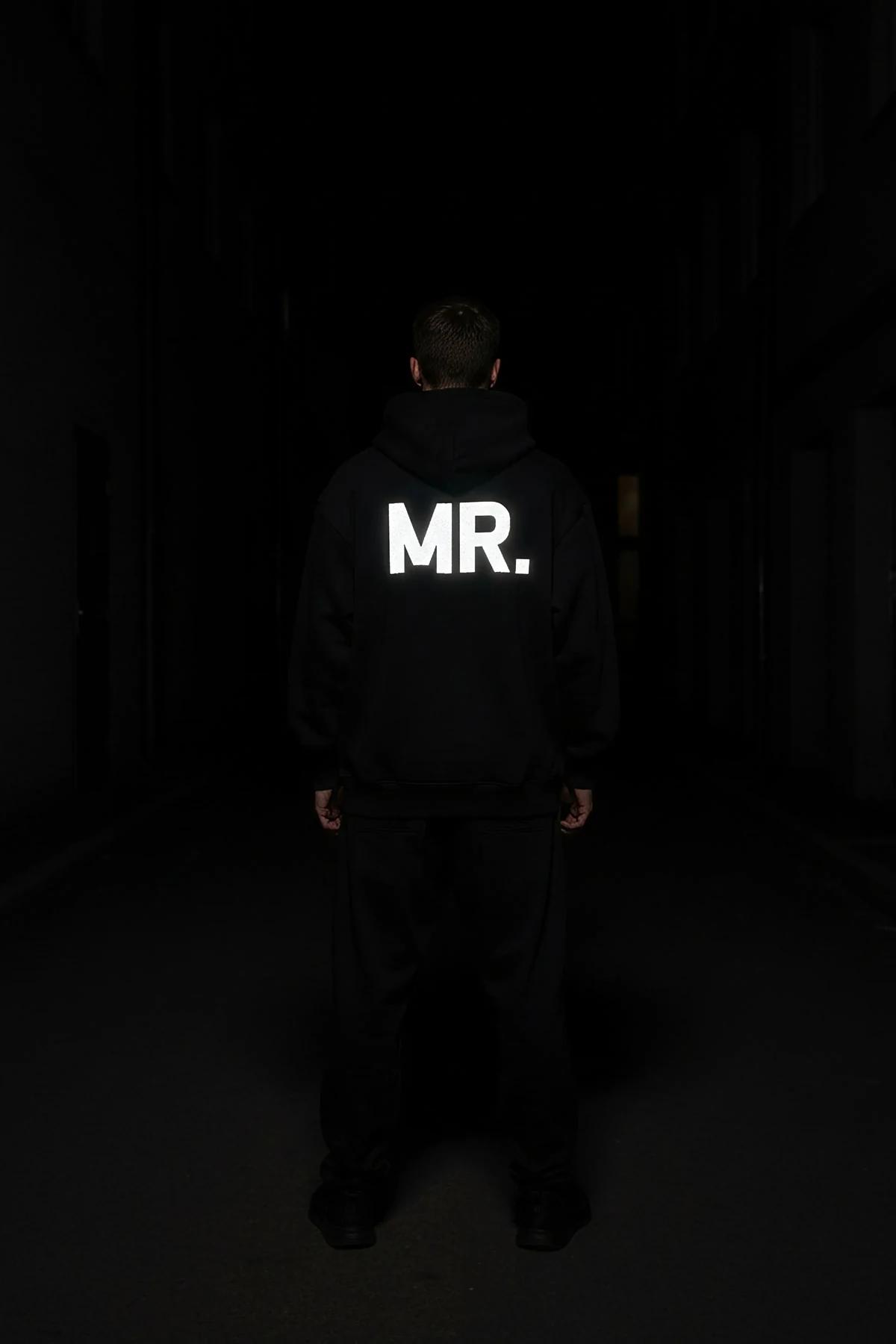 close-up of white MRS. block-letter print on left sleeve of black cotton-fleece hoodie in darkness