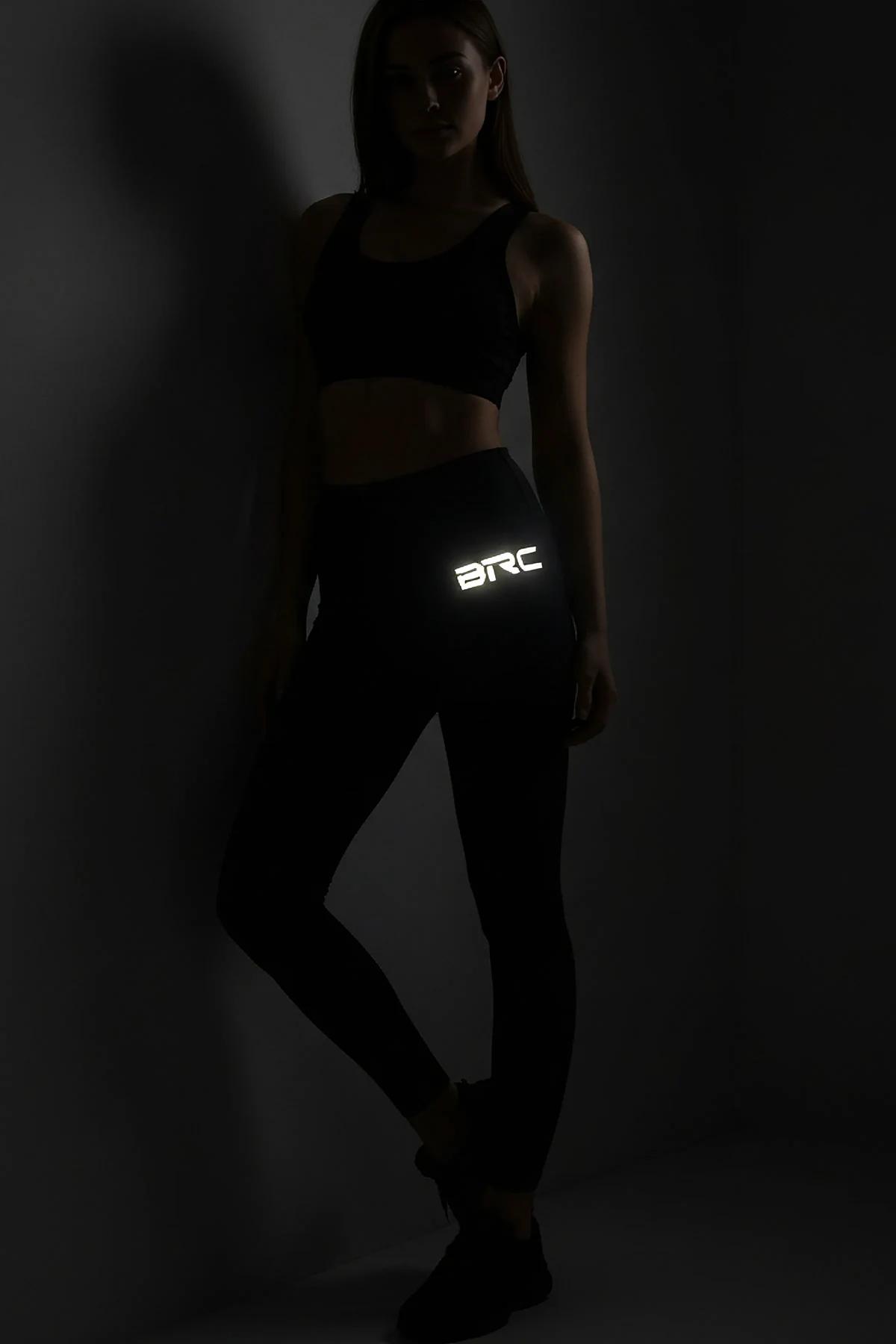 black high-waisted performance leggings with reflective logo print on outer thigh worn in dark gym setting