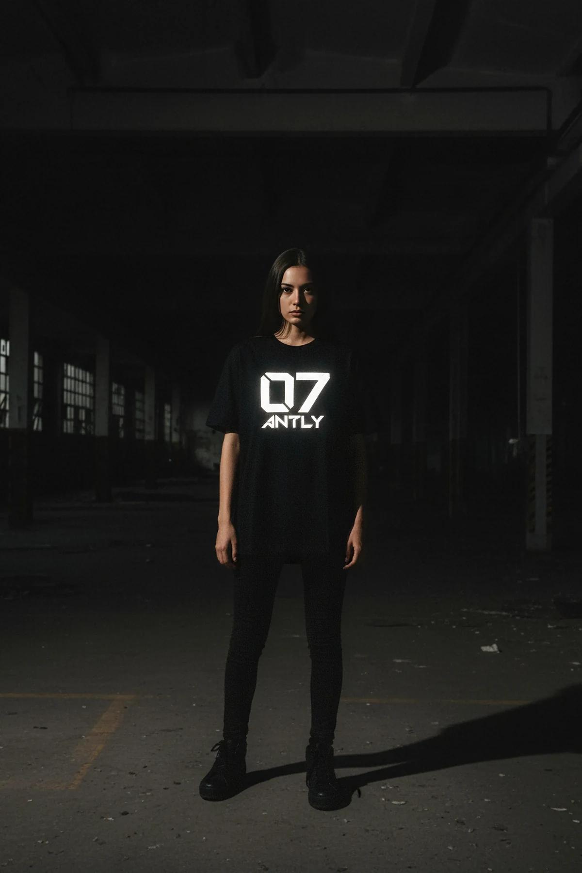 black oversized reflective graphic t-shirt with glowing white ANTLY 07 logo worn by woman in low light
