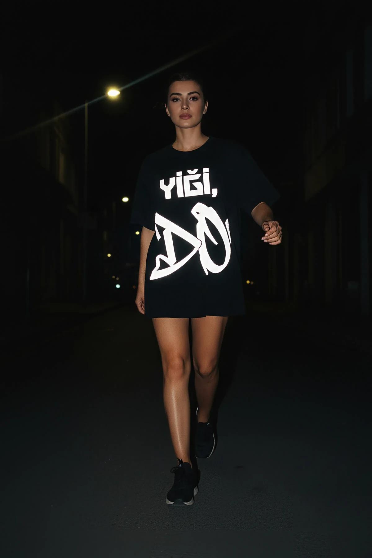 black reflective graphic t-shirt with bold white geometric typography print glowing in dark urban setting