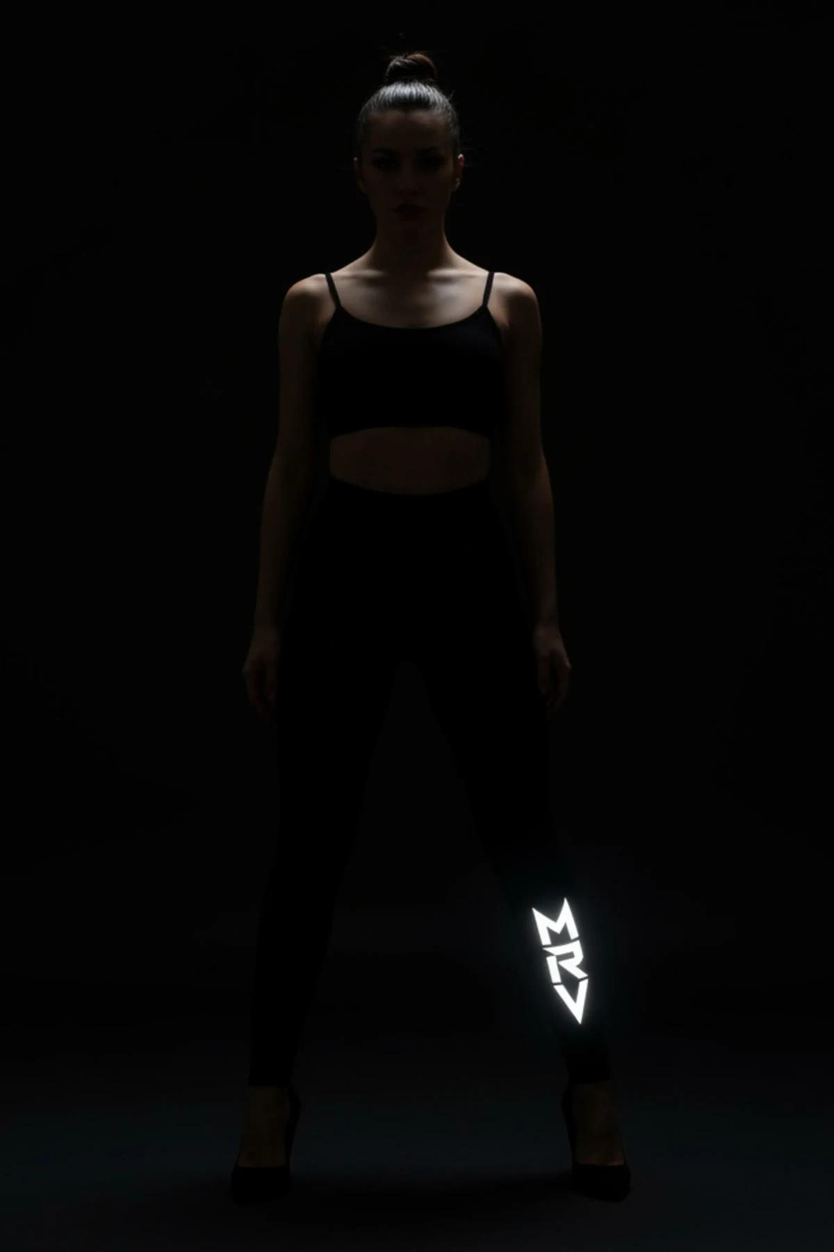 close-up of luminous white FT M brush-script logo on black leggings in dark outdoor setting