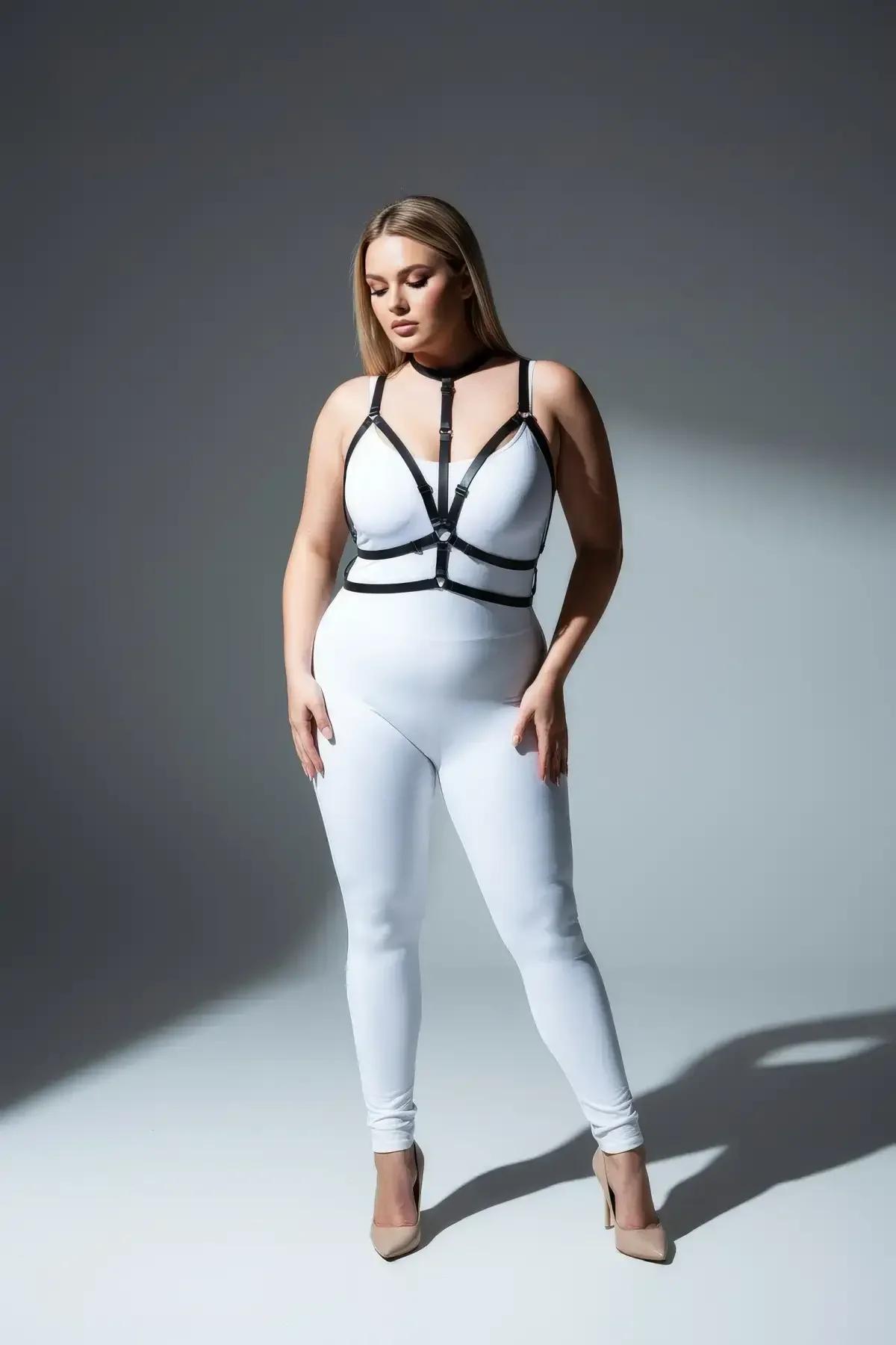 plus size model wearing black strappy body harness over white fitted outfit full length