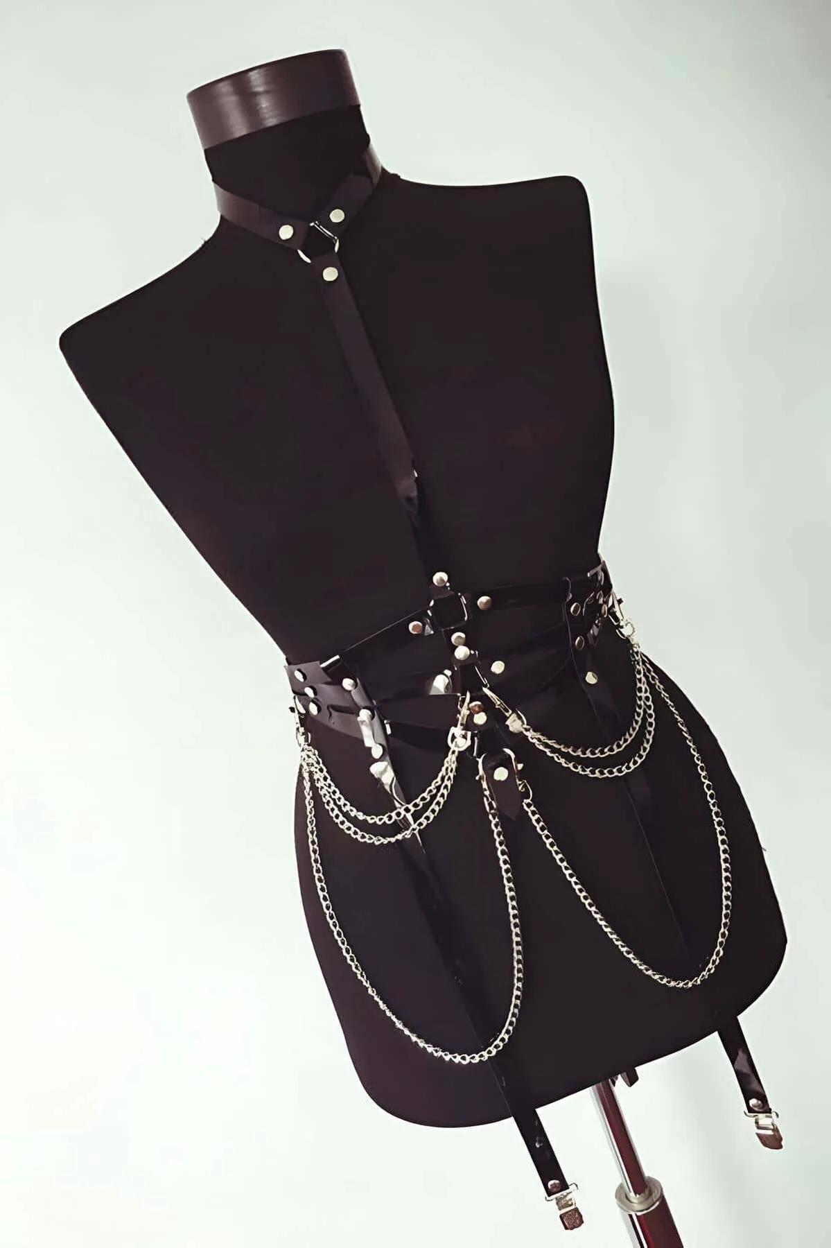 full torso view black faux leather cage harness with gold chain draping against dark background