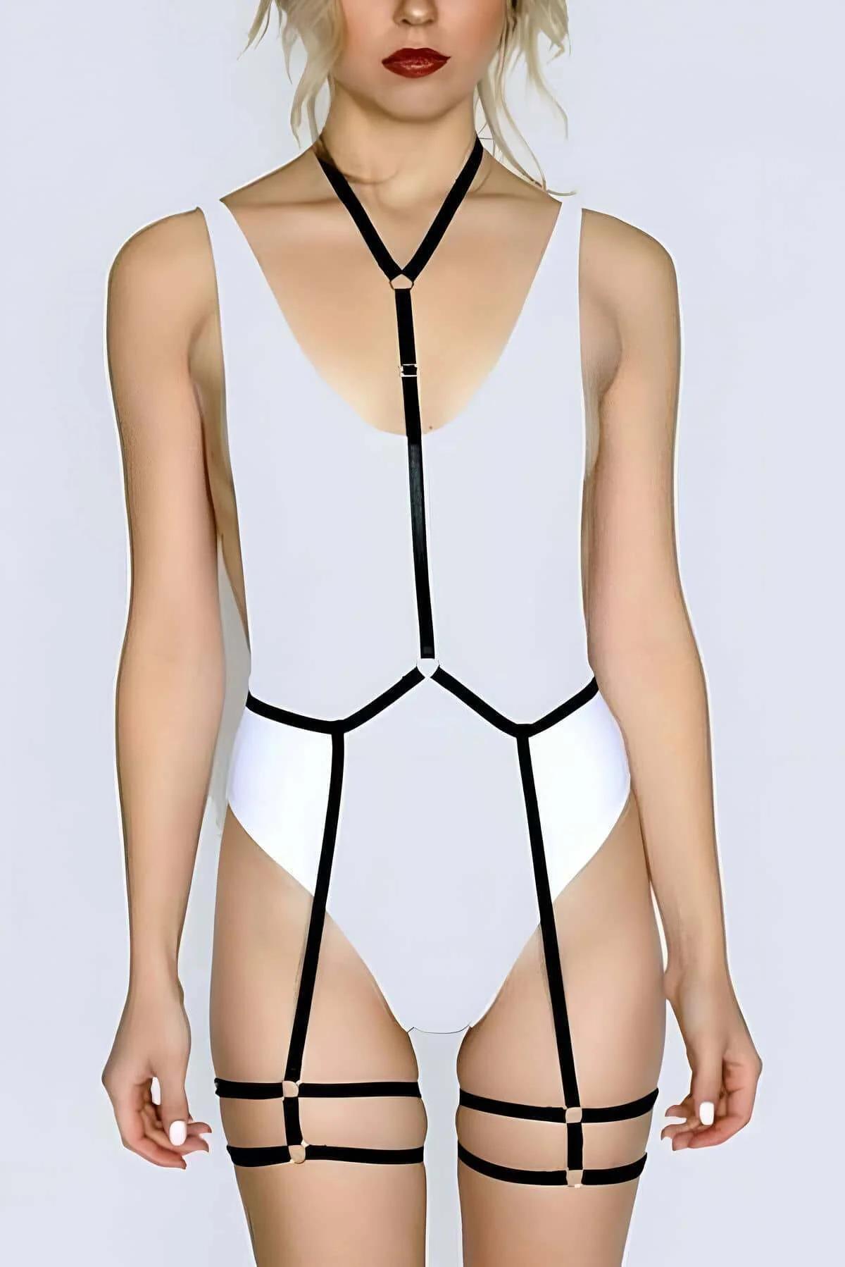 Siyah lastik full body harness çift bacak bantlı, altın O-ring göğüs halkası ve geometrik bel kafesiyle beyaz bodysuit üzerin