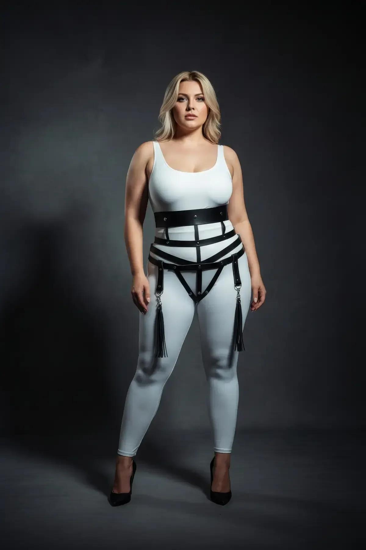 plus size model wearing black faux leather cage harness over white bodysuit with tassel garters hanging at thigh