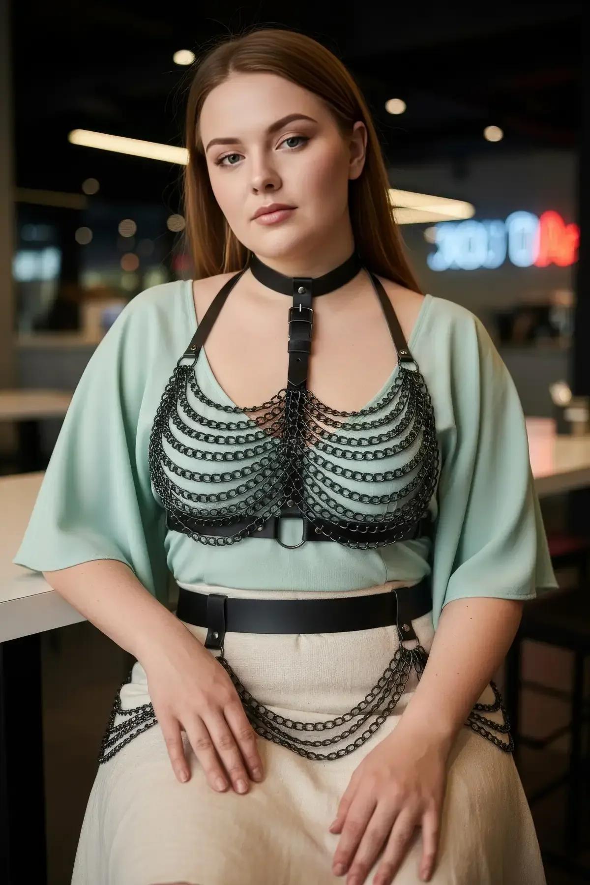 Black body harness with chain overlay layered over sage green sleeveless top and beige trousers