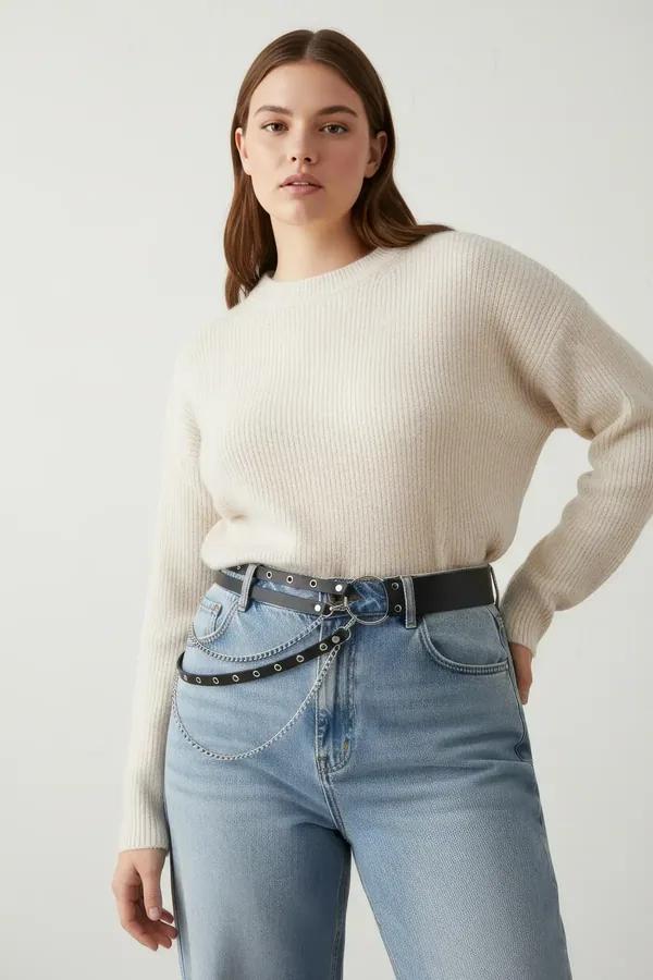 black faux leather double-row studded belt with silver O-ring and cascading chain drapes worn at waist over cream knit sweate