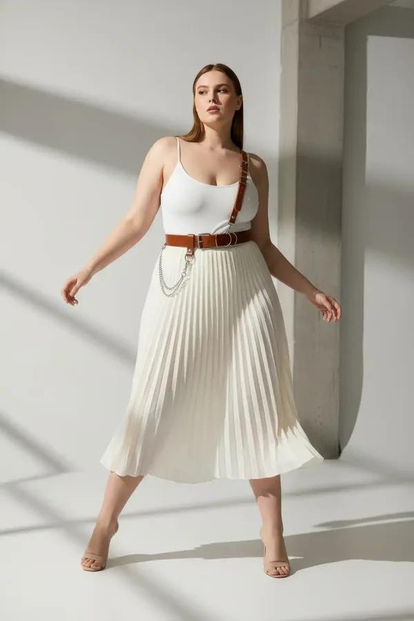 tan faux leather shoulder strap harness belt with silver D-ring buckles and draped chain detail worn over white bodysuit
