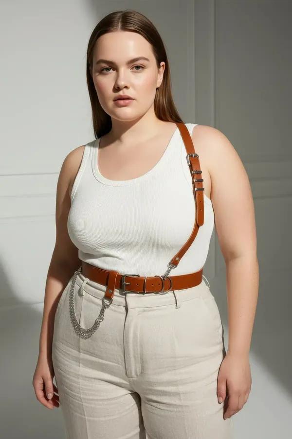 tan faux leather shoulder strap harness belt with silver D-ring buckles and draped chain detail worn over white bodysuit