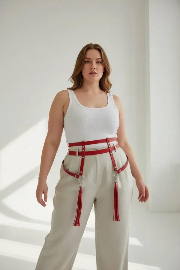 Red faux leather waist harness with silver O-rings and detachable red tassel thigh straps worn over cream trousers