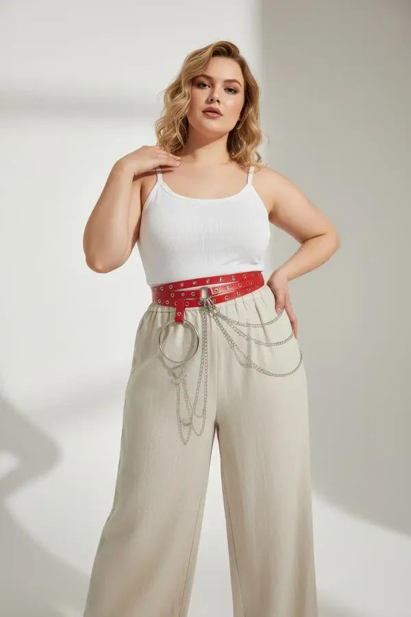 red faux leather belt with large silver O-ring and draped chain detail worn at natural waist over cream trousers