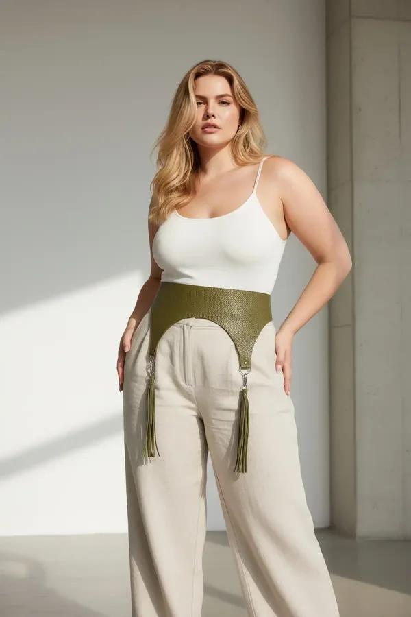 olive green high-waisted underbust harness belt with silver O-ring hardware and matching tassel garters worn over linen trous
