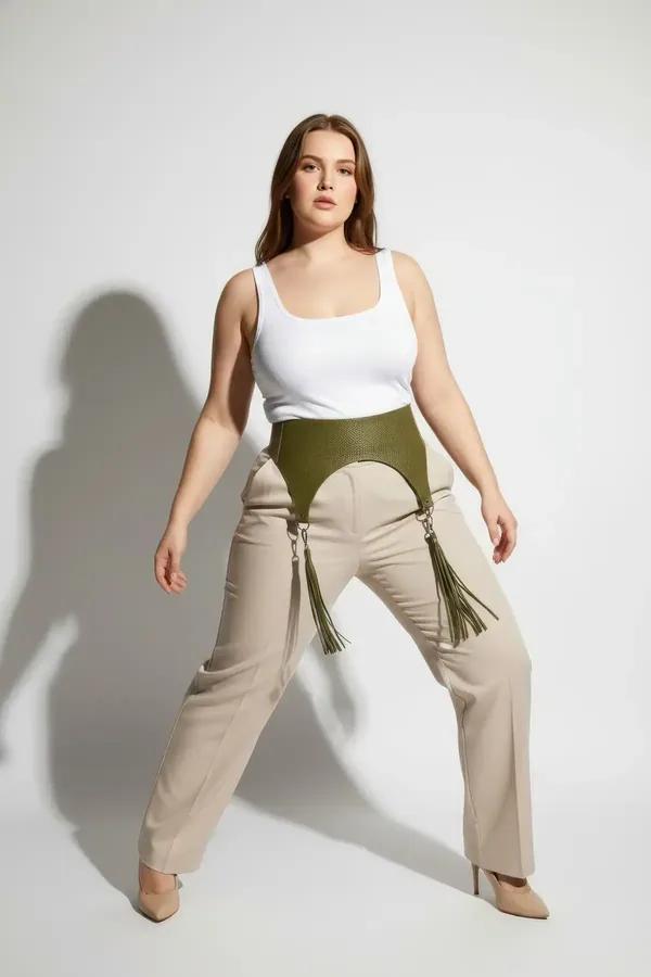 olive green high-waisted underbust harness belt with silver O-ring hardware and matching tassel garters worn over linen trous