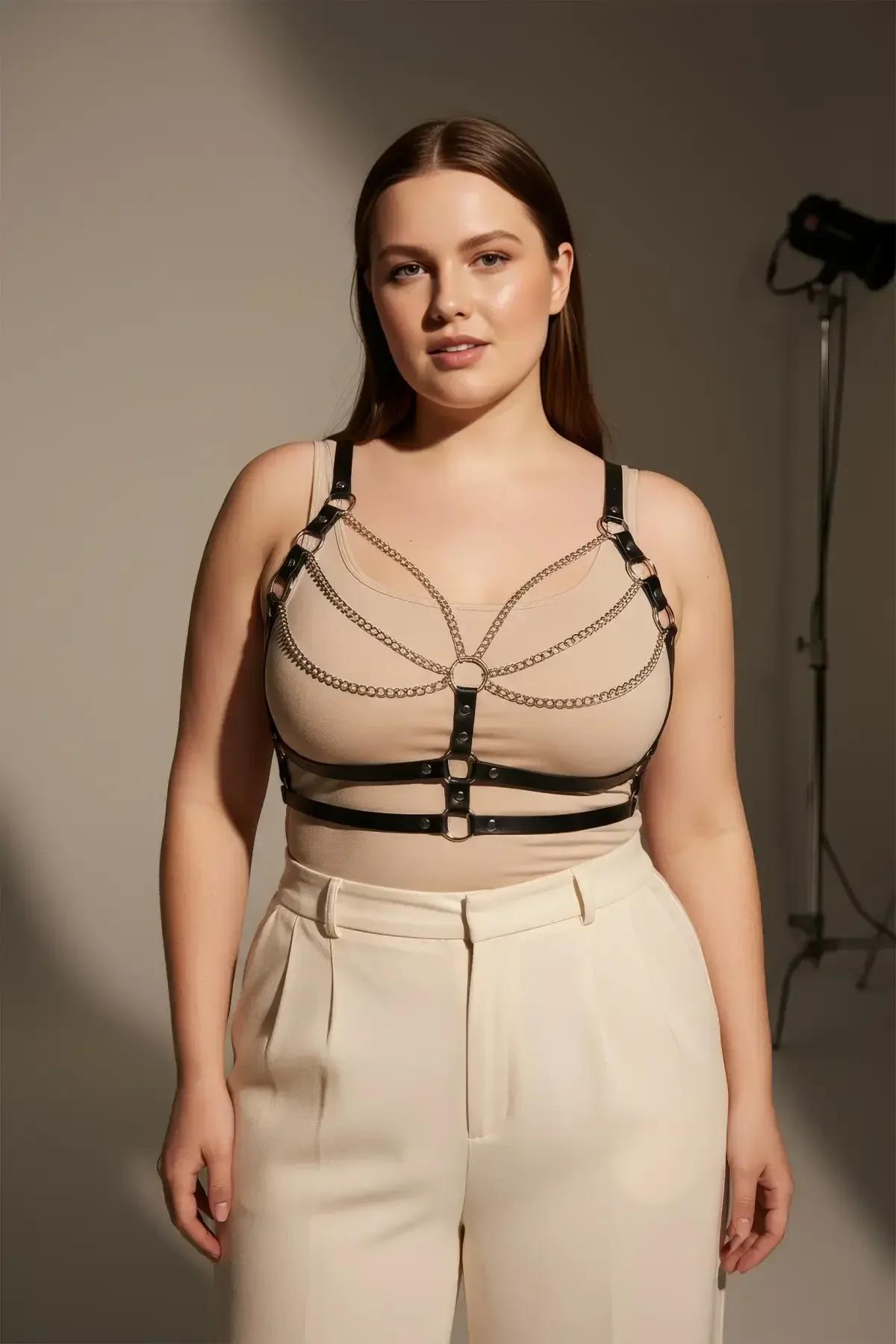 plus-size model wearing black faux leather harness bra with silver chain detail and wide-leg trousers