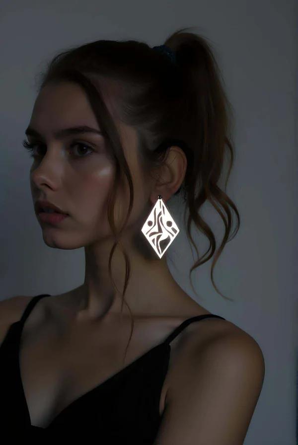 Gümüş renkli elmas formlu reflektörlü lazer kesim geometrik küpe, tribal motifli metalik yüzey, model kulağında