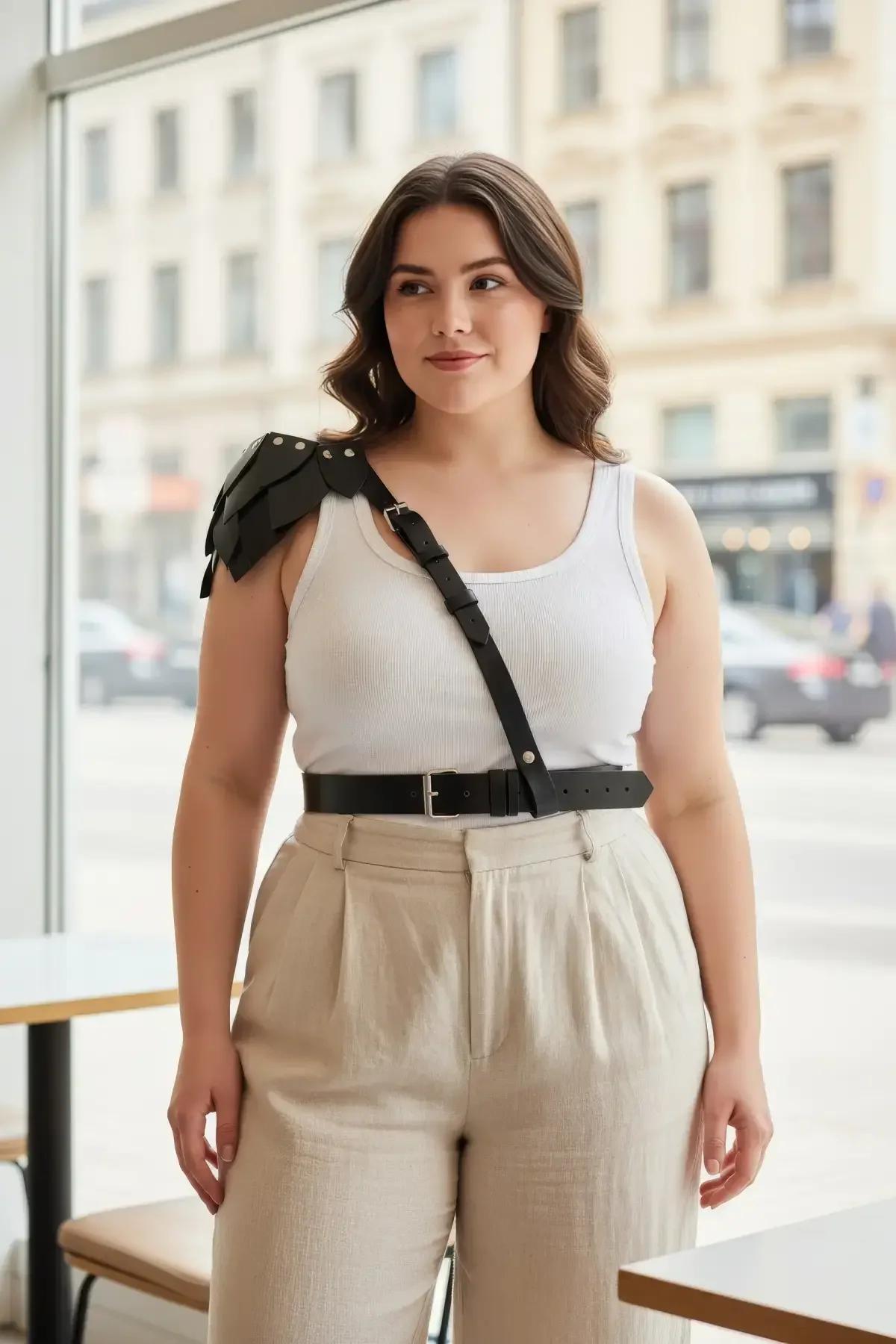 Black faux leather shoulder harness with tiered epaulette and wide waist belt worn over white tank top