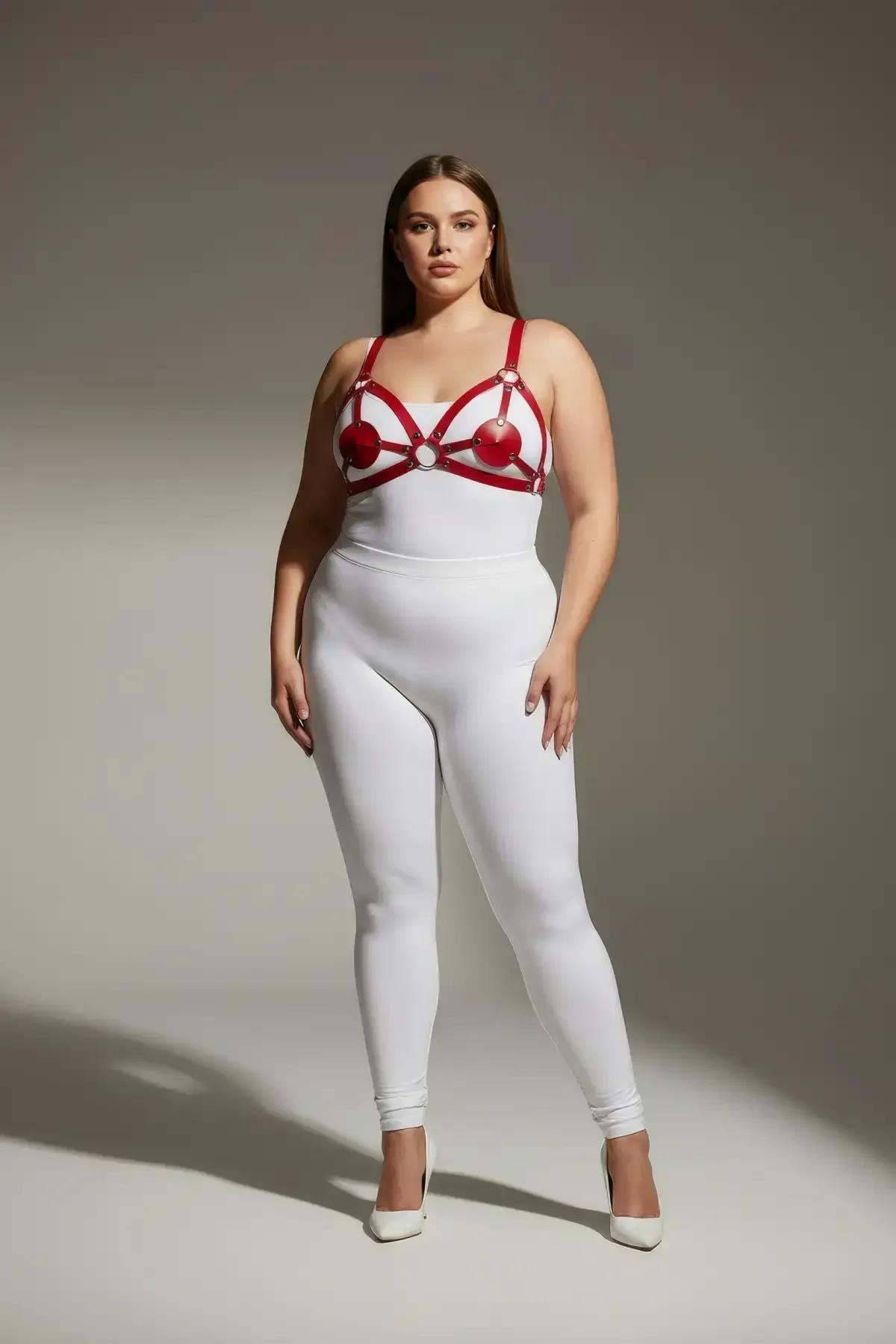 Red strappy chest harness with heart-shaped cup panels and silver O-ring on plus-size model over white bodysuit