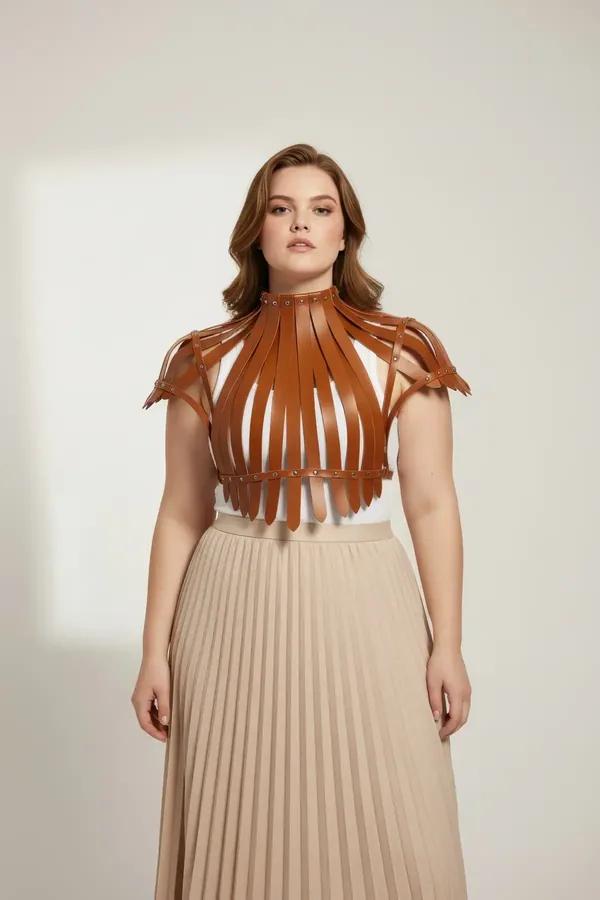 tan faux leather high-neck harness top with radiating straps and gold dome studs worn over cream bodysuit