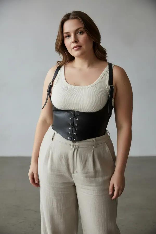 black faux leather underbust corset harness with front lace-up and silver buckle shoulder straps worn over cream top