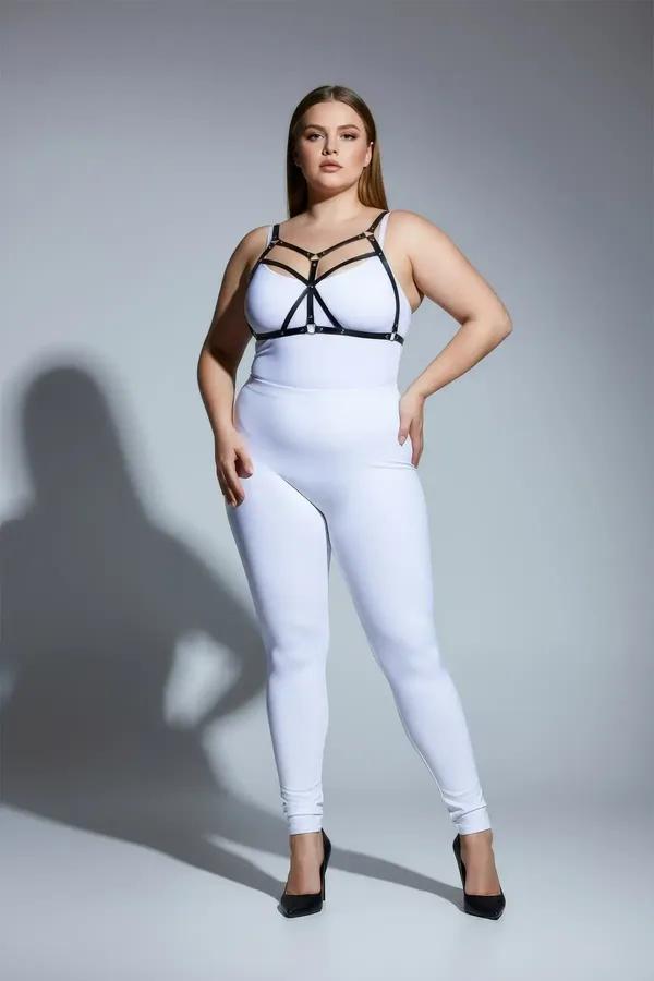 Strappy black faux leather body harness with gold O-ring hardware worn over white bodysuit, cage-style chest strap design