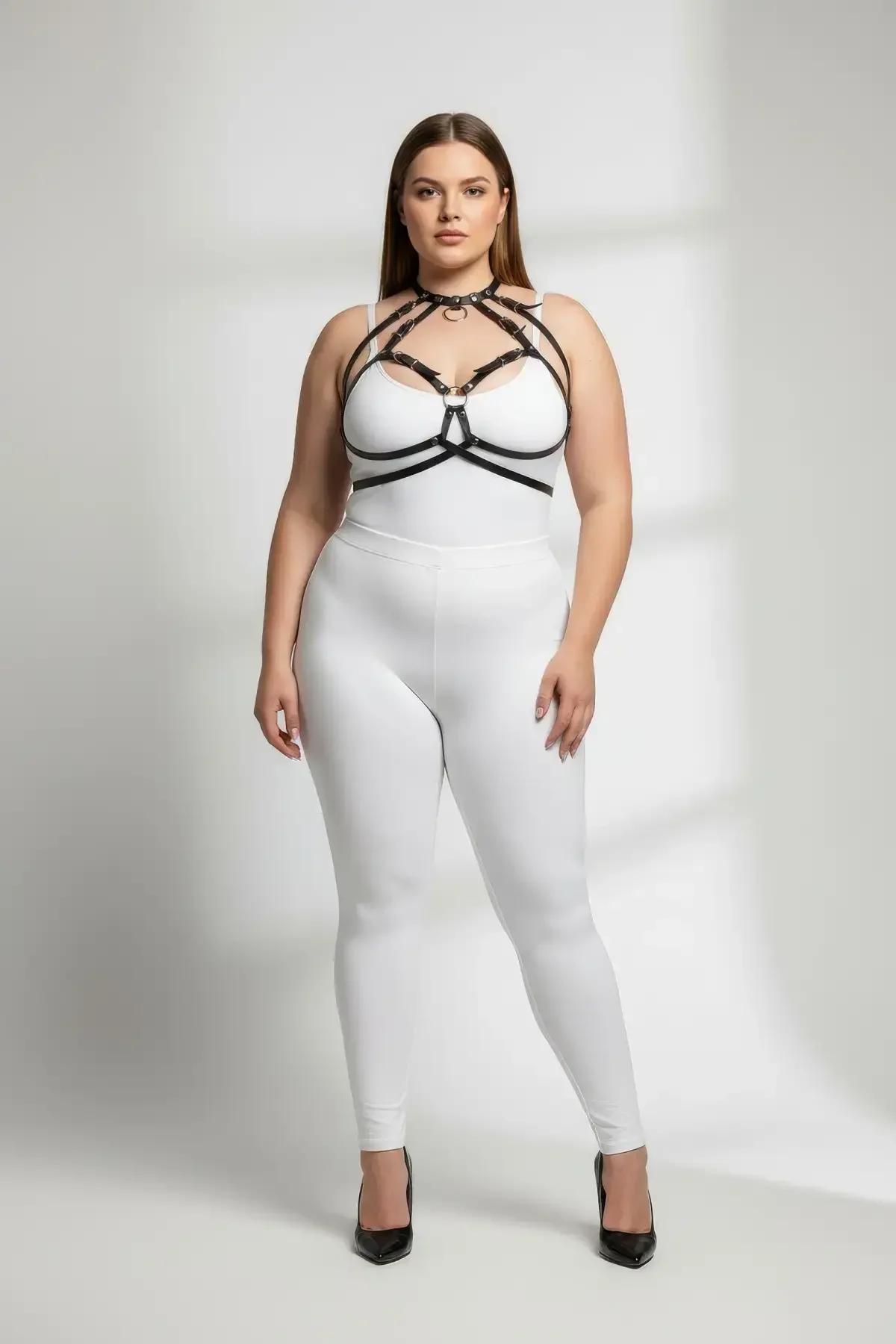 black faux leather strappy o-ring chest harness with gold buckles worn over white bodysuit plus size model