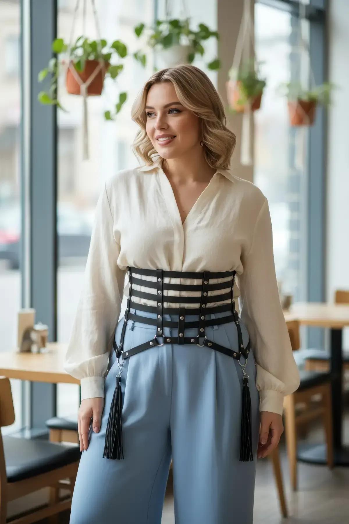black faux leather corset waist harness with five stacked straps silver rivets and detachable tassels worn over cream blouse