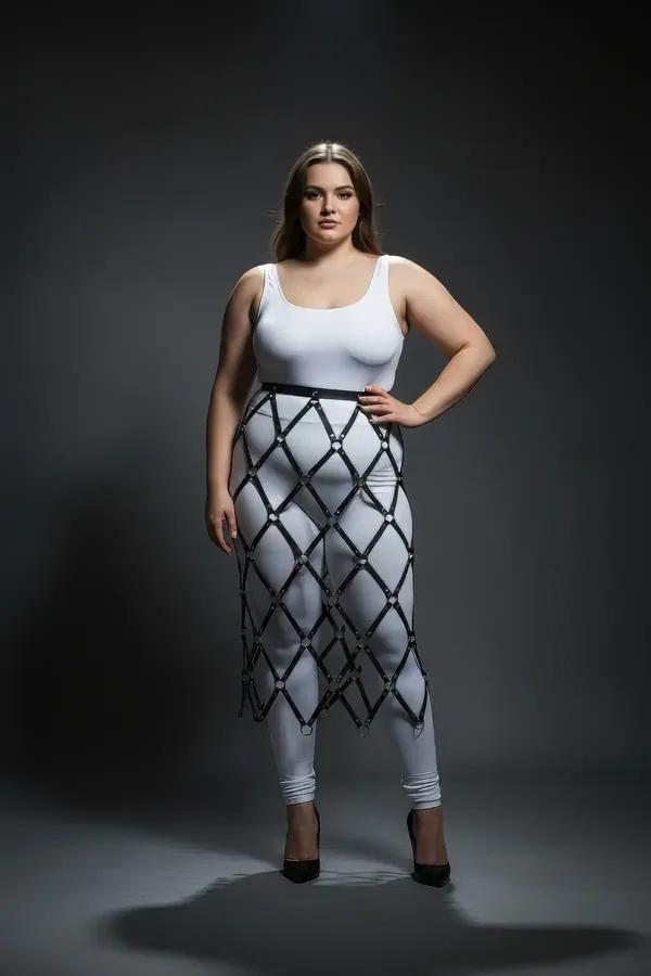 Black faux leather diamond lattice skirt harness with silver O-rings at every strap intersection, worn over white leggings