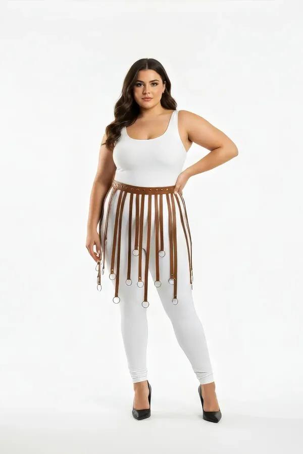 Tan faux leather fringe skirt harness with silver O-ring tipped straps worn over white leggings, plus size model