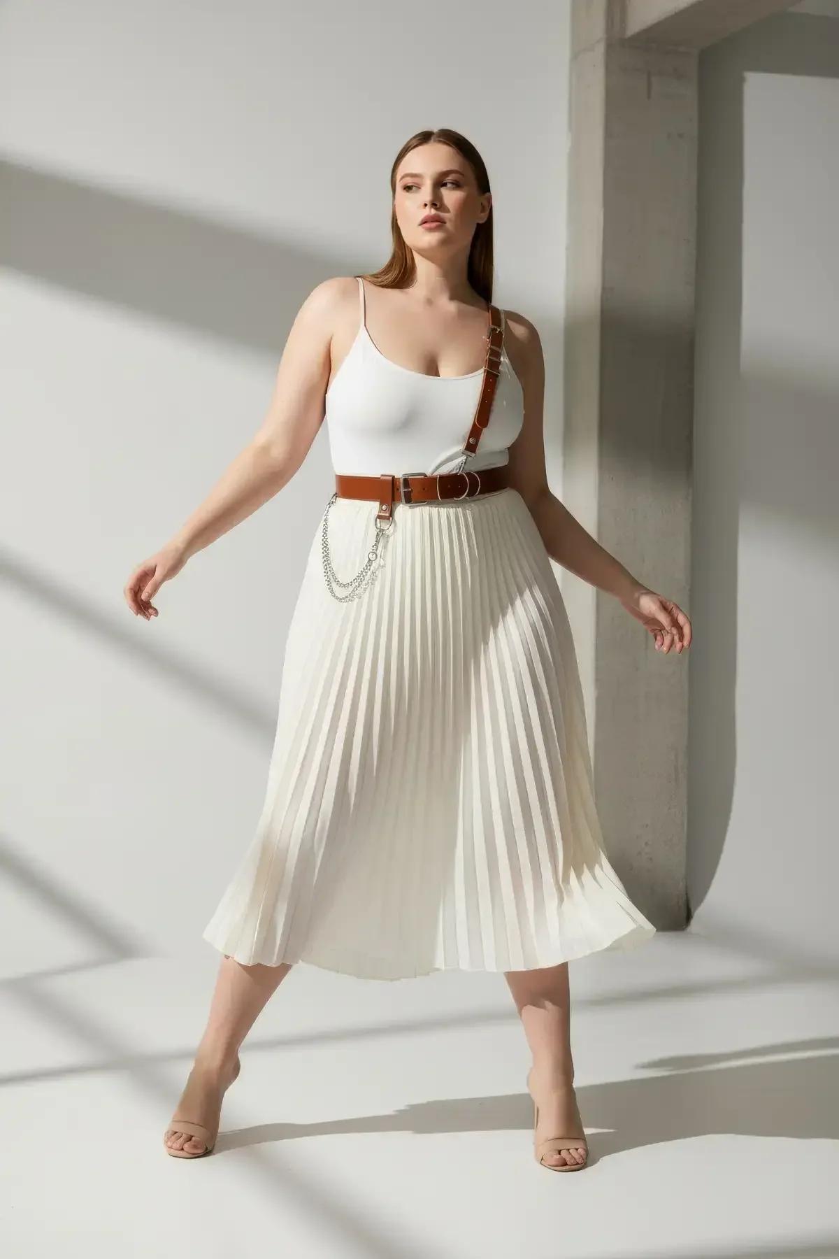 tan faux leather shoulder strap harness belt with silver D-ring buckles and draped chain detail worn over white bodysuit
