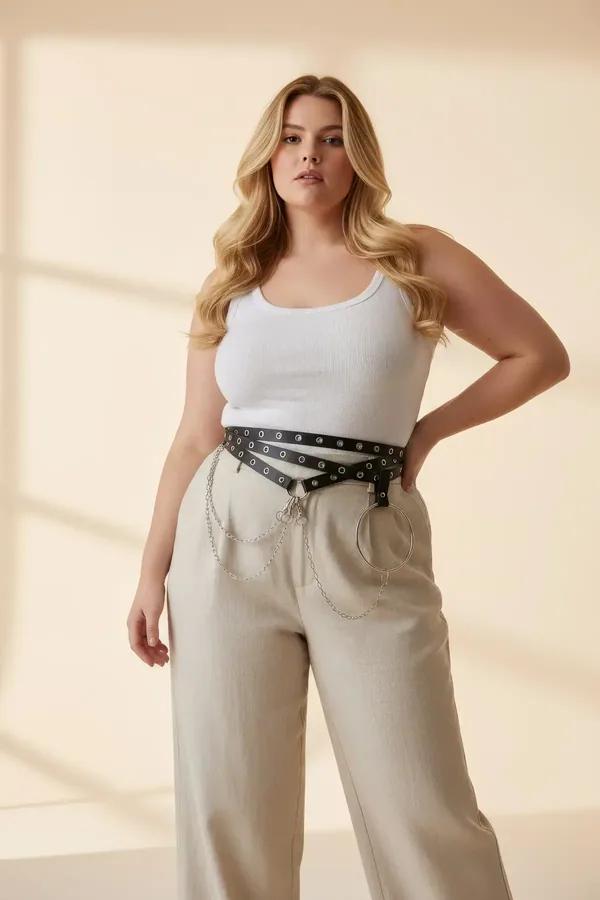 black faux leather waist harness with silver grommets, large O-ring and draped chain detail worn over wide-leg trousers