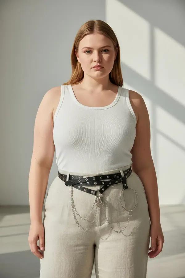 black faux leather waist harness with silver grommets, large O-ring and draped chain detail worn over wide-leg trousers