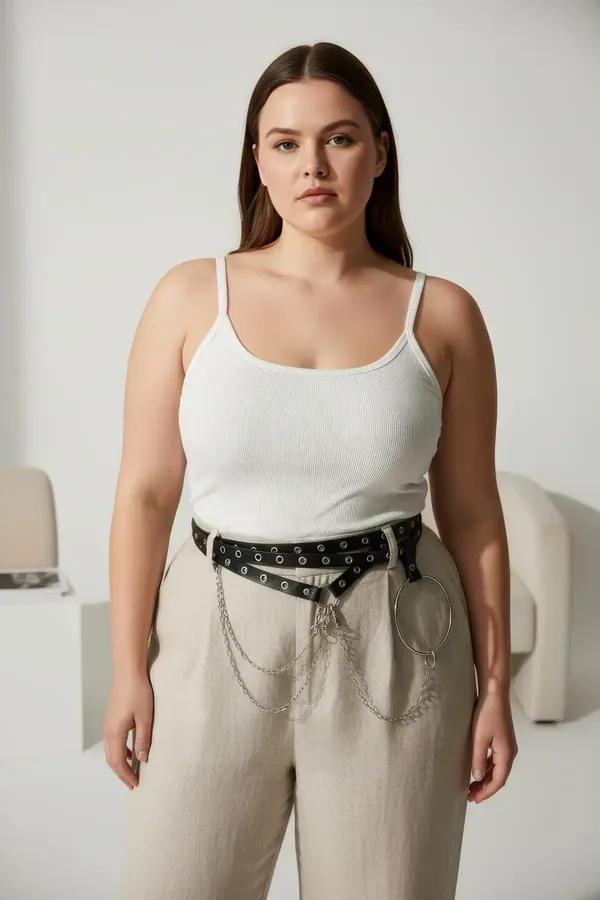 black faux leather waist harness with silver grommets, large O-ring and draped chain detail worn over wide-leg trousers