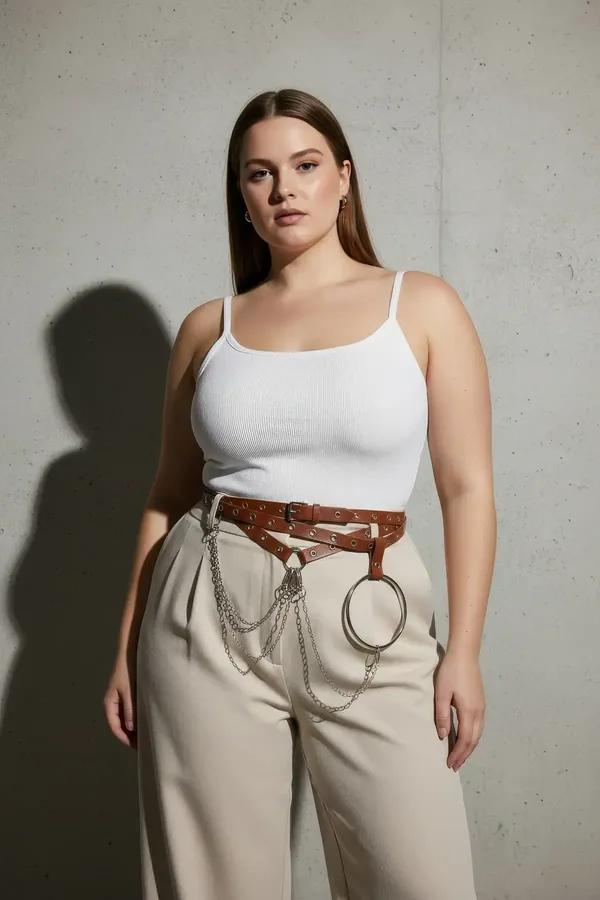 Brown faux leather waist harness belt with silver grommets draped chains and O-ring worn over white top and cream maxi skirt
