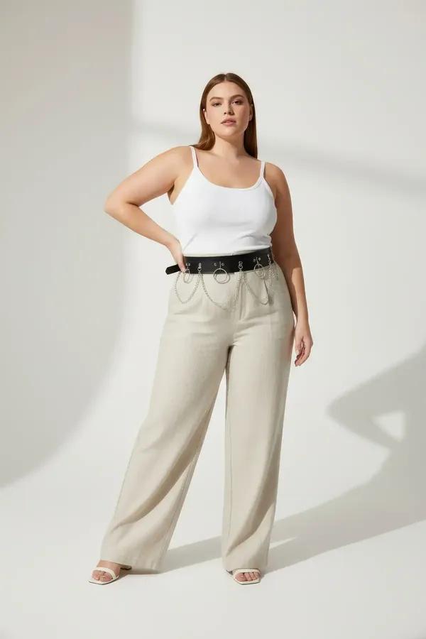 Black faux leather harness belt with four silver O-rings and draped chain links worn at the waist over wide-leg trousers