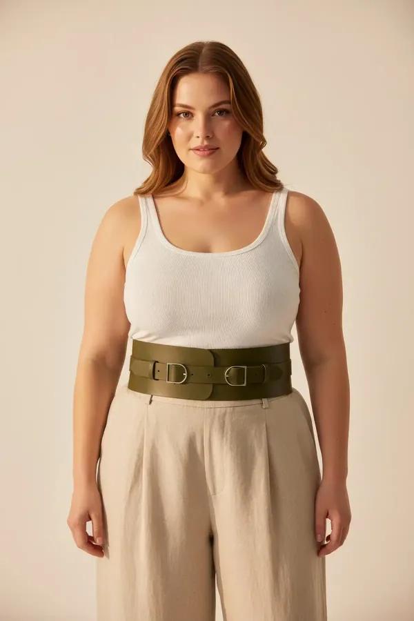 wide olive green vegan leather waspie waist belt with double silver D-ring buckles worn over white tank and beige trousers