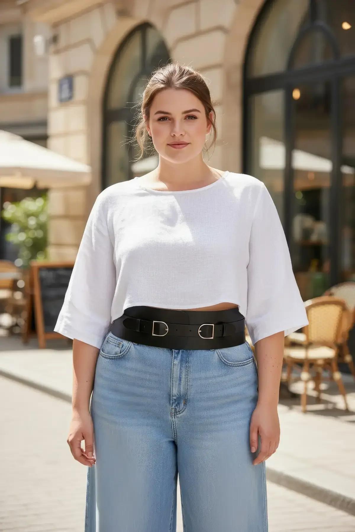 black wide faux leather waist harness belt with two silver D-ring buckles worn over white crop top and jeans