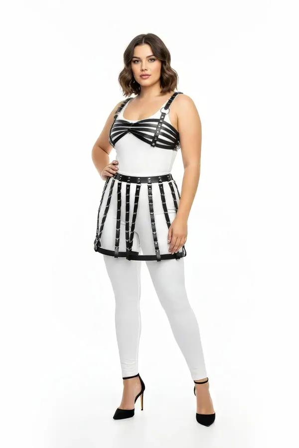 Black faux leather cage harness skirt with silver rivets on waistband worn over white leggings, vertical strap construction