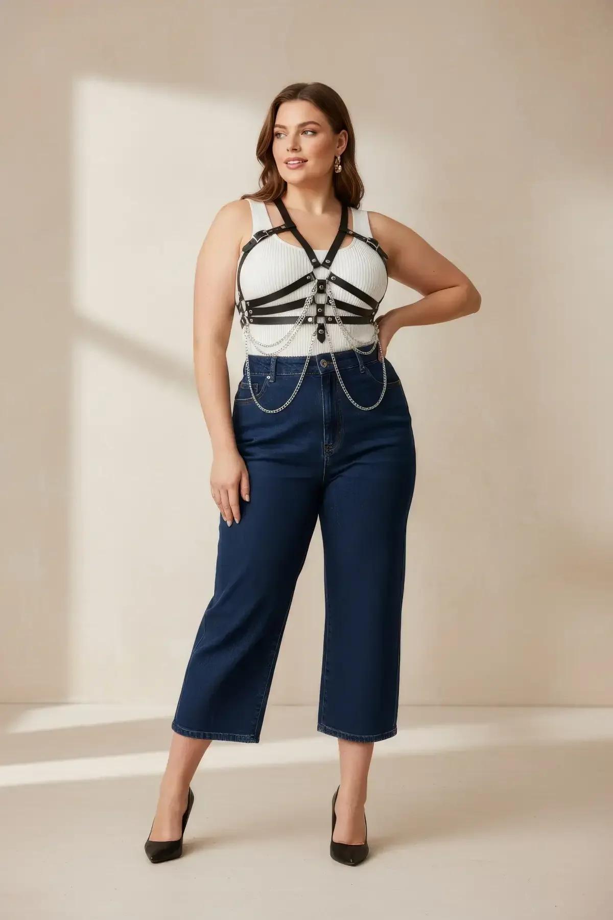 black faux leather full body harness with silver draping chains and metal O-rings worn over white ribbed tank and jeans