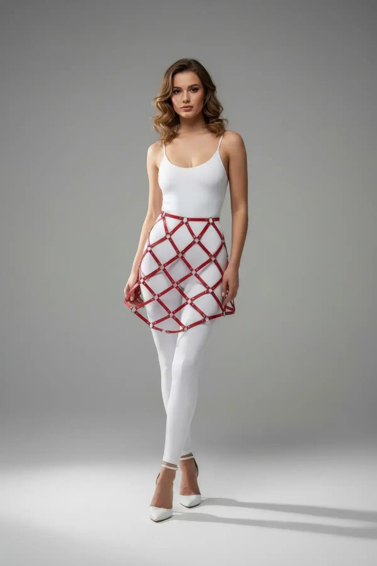 Red faux leather lattice skirt harness with silver stud intersections worn over white bodysuit and leggings