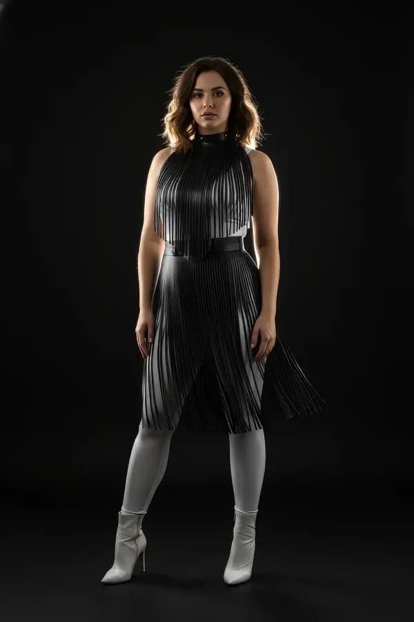 Black vegan leather fringe overlay harness dress with high mock neck collar and cinching waist belt, midi length