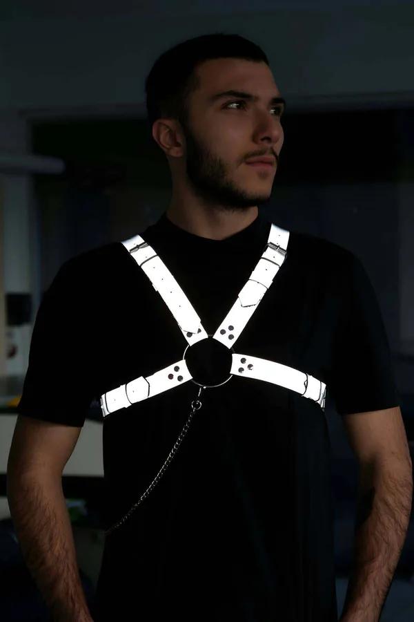 Reflektörlü gri erkek göğüs harness, ışık altında beyaz-gümüş parıltı, siyah O-ring ve metal zincir detayı