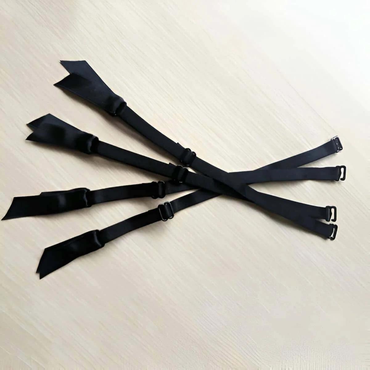 Four black adjustable garter straps fanned on light wood surface, showing silver-tone metal slide adjusters and hook clasps,
